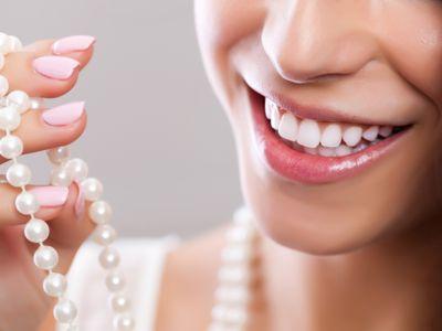 Foto einer jungen Frau mit wei&szlig;en Z&auml;hnen und einer Perlenkette in der Hand
