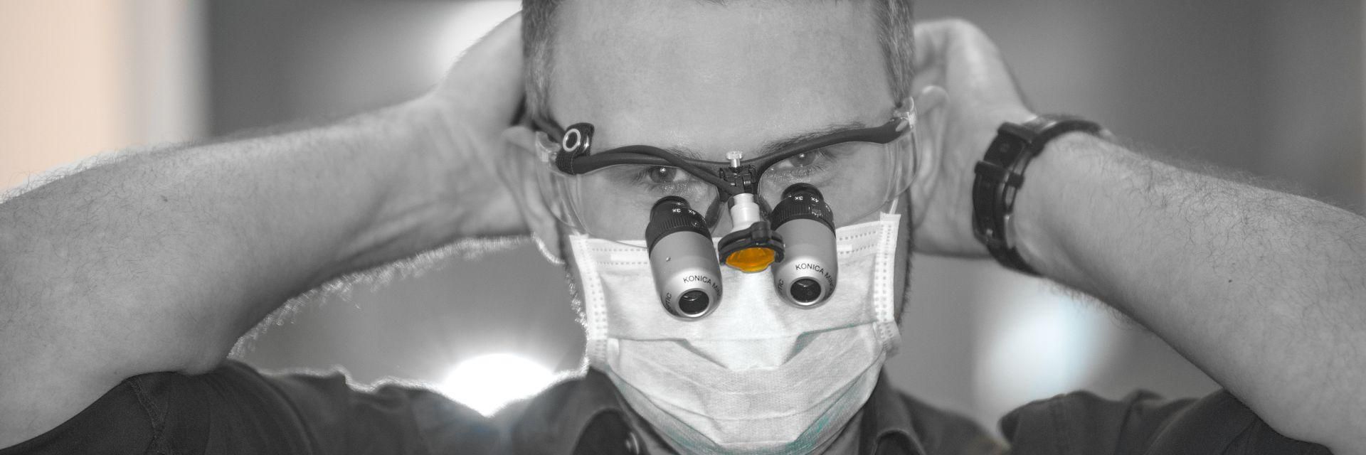 A black-and-white photo of a dentist with magnifying glasses